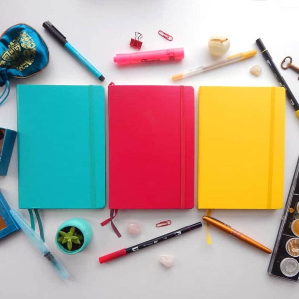 turquoise, red and yellow bullet journals laying in a row