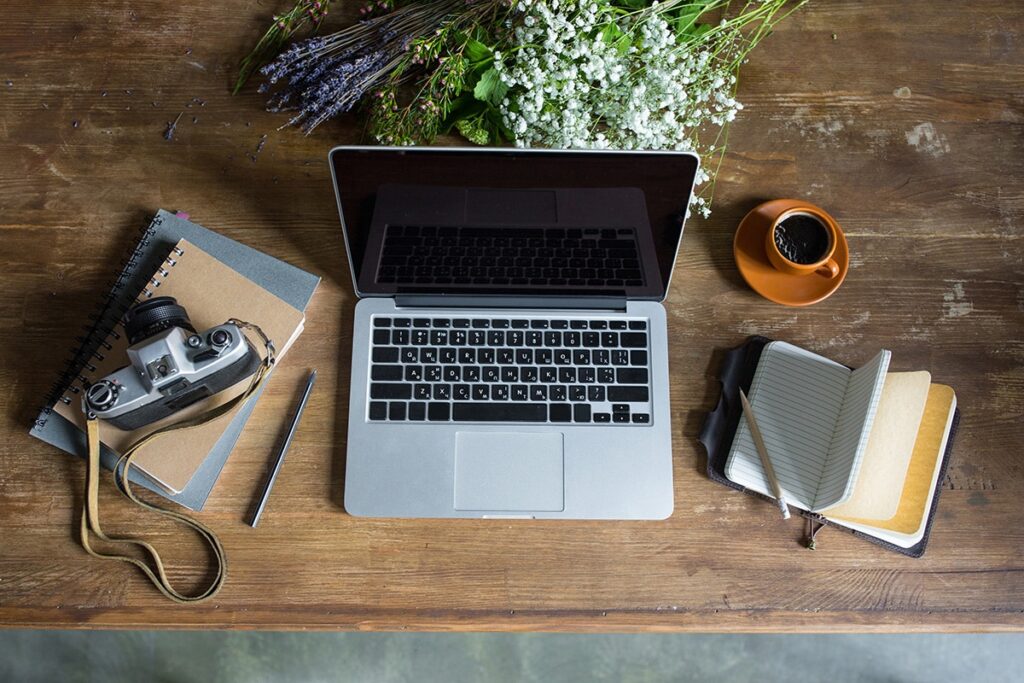 top view of laptop, diaries, vintage photo camera and cup of coffee