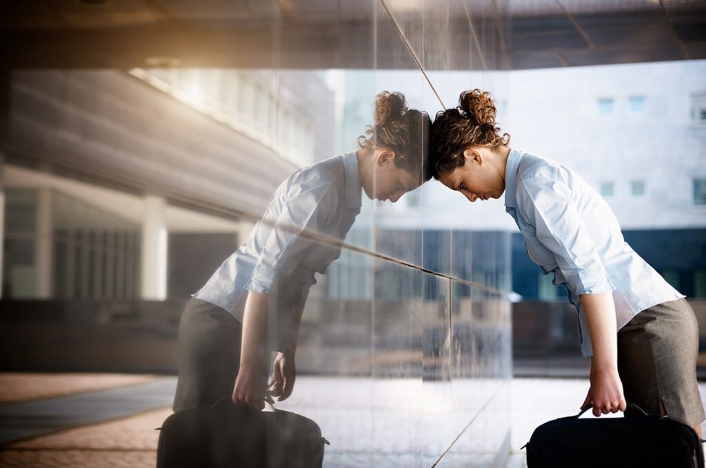 Woman leaning on building looking sad because she feels impostor syndrome