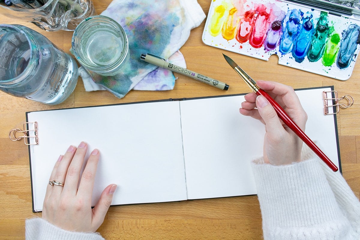 Watercolor sketchbook on table with watercolors