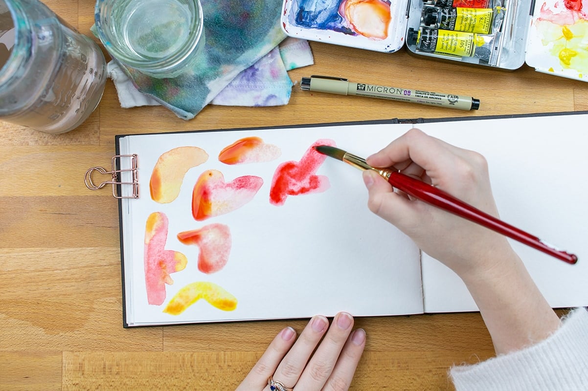 Hand painting red watercolor blobs on page.