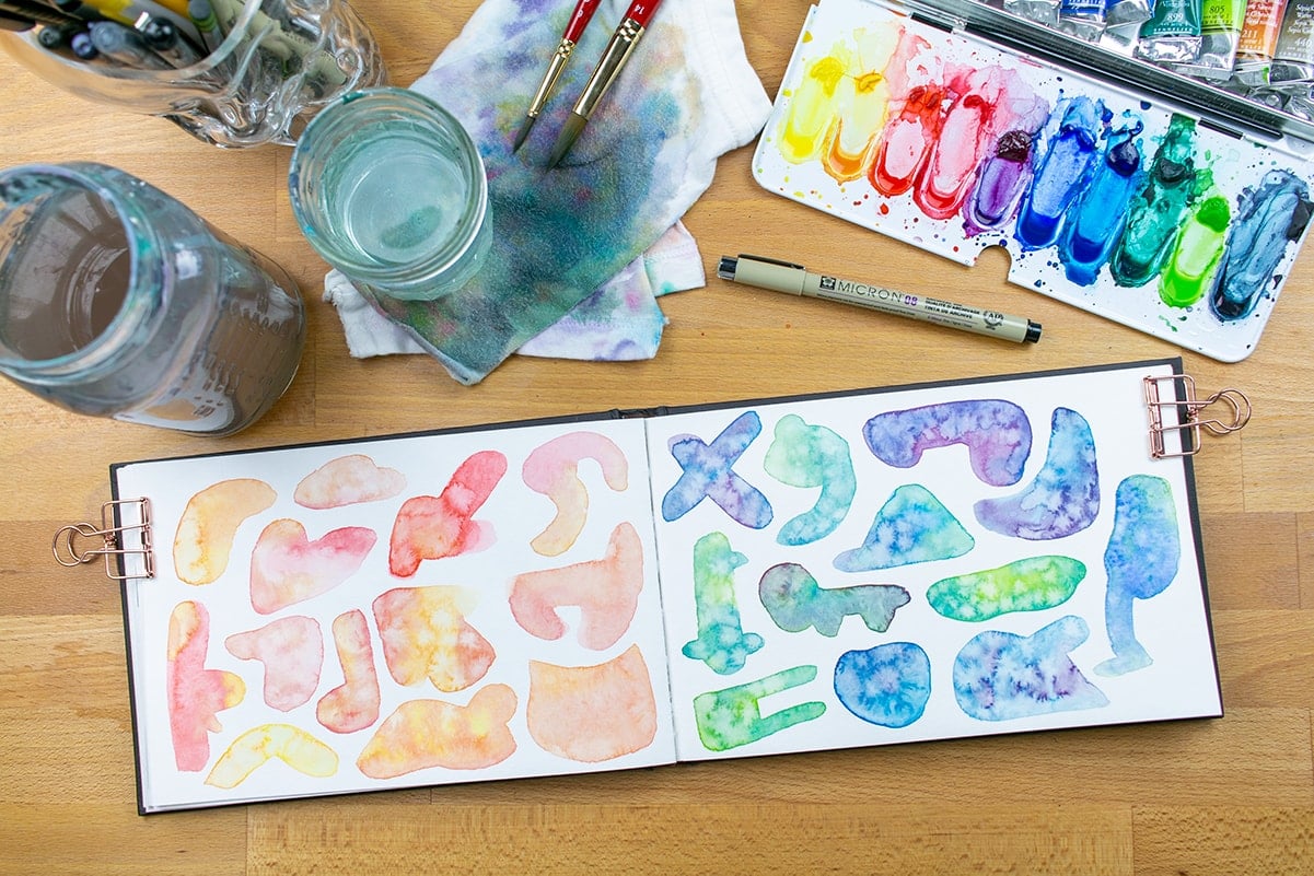 Both pages of warm and cool paint shapes on desk with paint supplies.