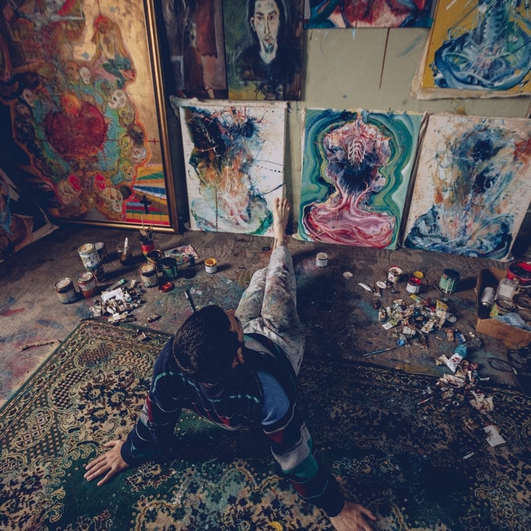 man sitting in front of his paintings